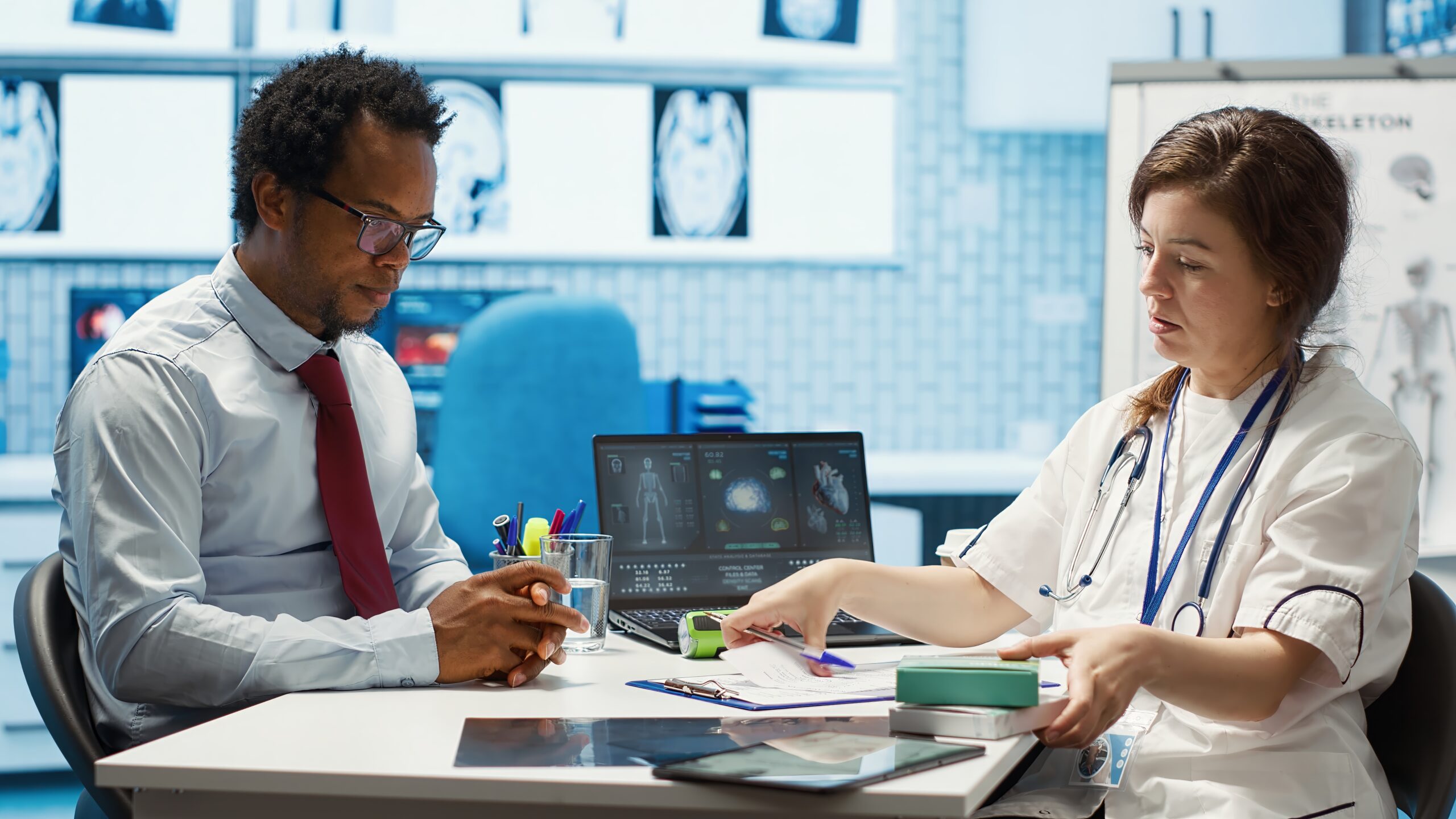 A male patient discusses comprehensive primary healthcare with a female doctor, who is showing him documents on a clipboard